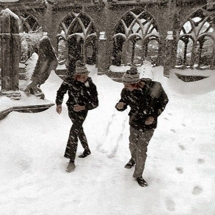 two people walking through the snow in front of an old building