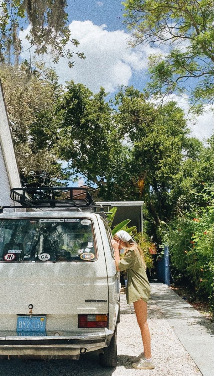 a woman standing next to a white van on the side of a road in front of a house