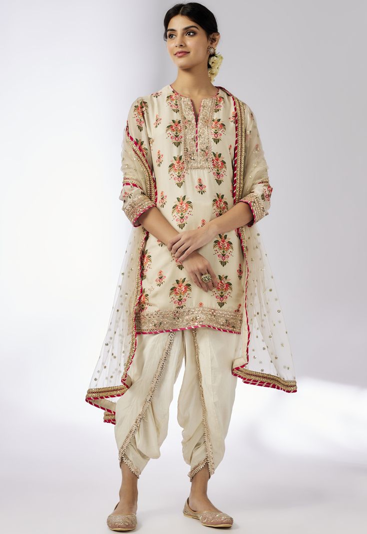 This pretty ensemble in floral jaal, combines gota and dori buttis with an intricate border embroidery. The short kurta with a dhoti embroidered in sequins and gold thread, adds a feminine grace. Off White Saree Set With Gota Work, Festive Off-white Gota Work Sets, Cream Salwar Kameez With Gota Work, Traditional Cream Salwar Kameez With Gota Work, Traditional Drape Sets With Floral Embroidery In Cream, Cream Sets With Floral Embroidery And Traditional Drape, White Anarkali Sherwani With Floral Embroidery, Festive Cream Kurta With Gota Work, Cream Kurta With Gota Work In Traditional Style