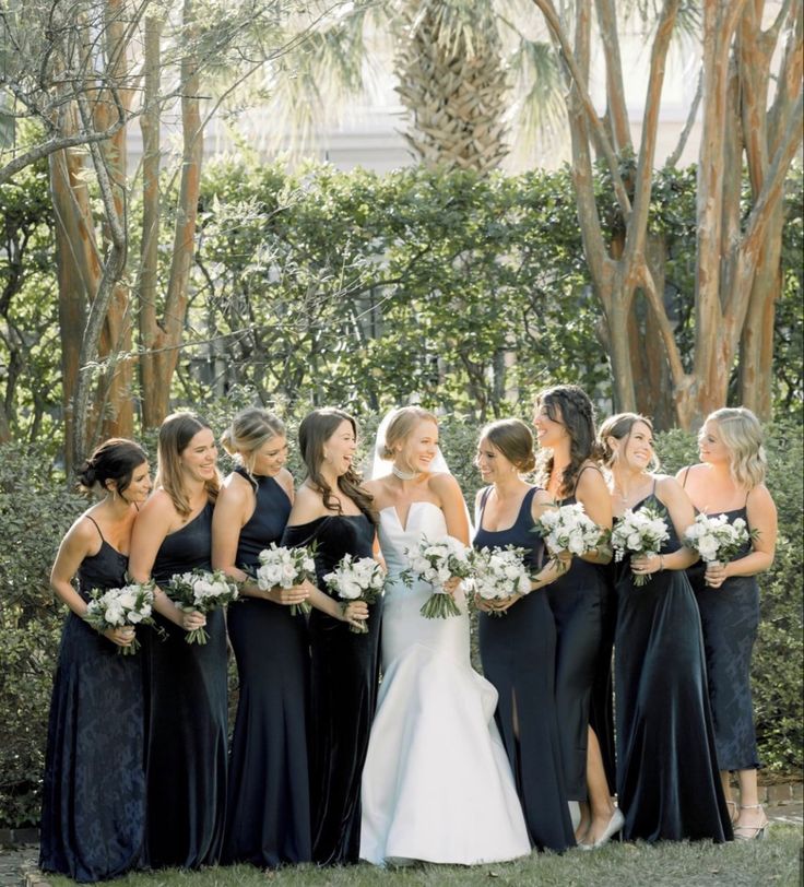 a group of women standing next to each other in front of some trees and bushes