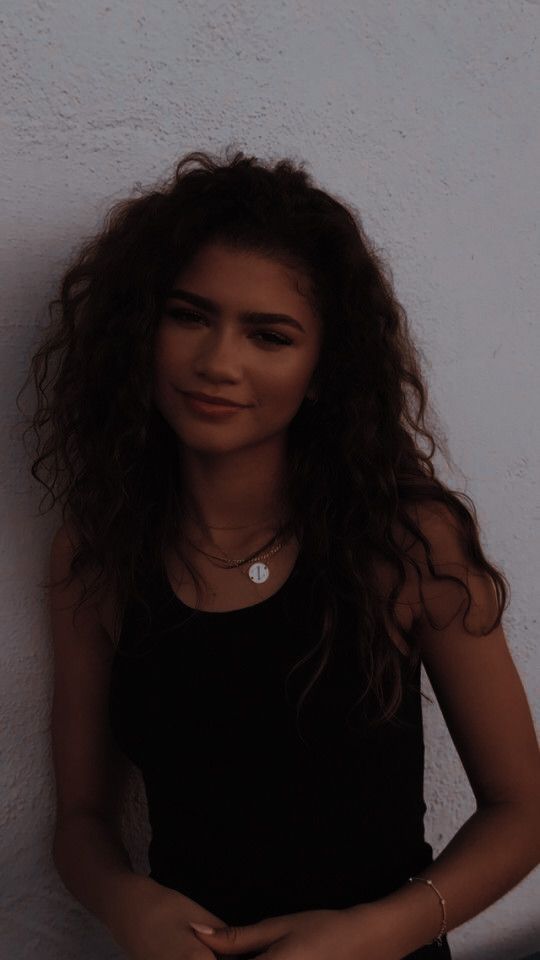 a woman with long hair standing against a white wall