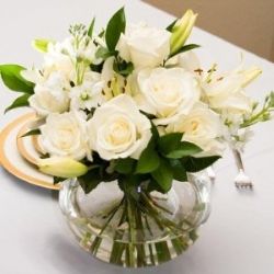 a vase filled with white flowers sitting on top of a table next to a plate