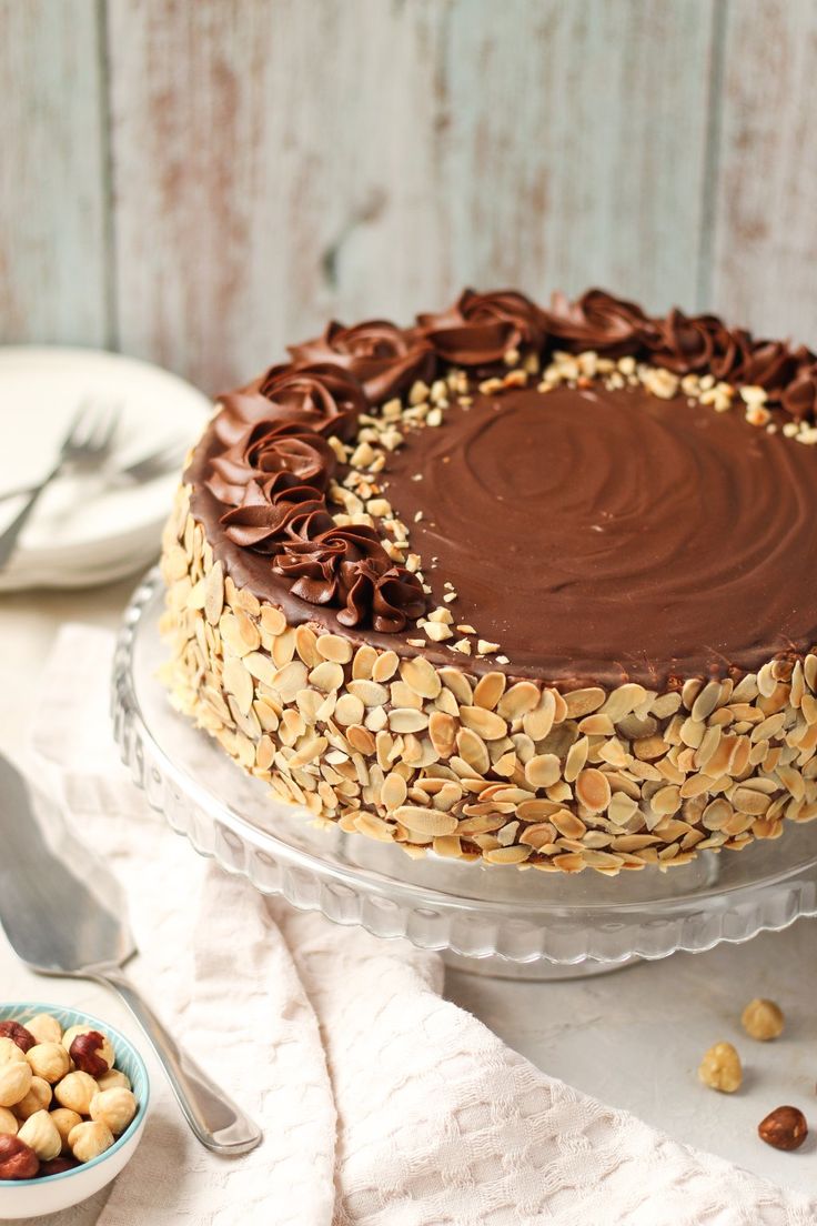 a chocolate cake with nuts on top sitting on a table next to a bowl of nuts