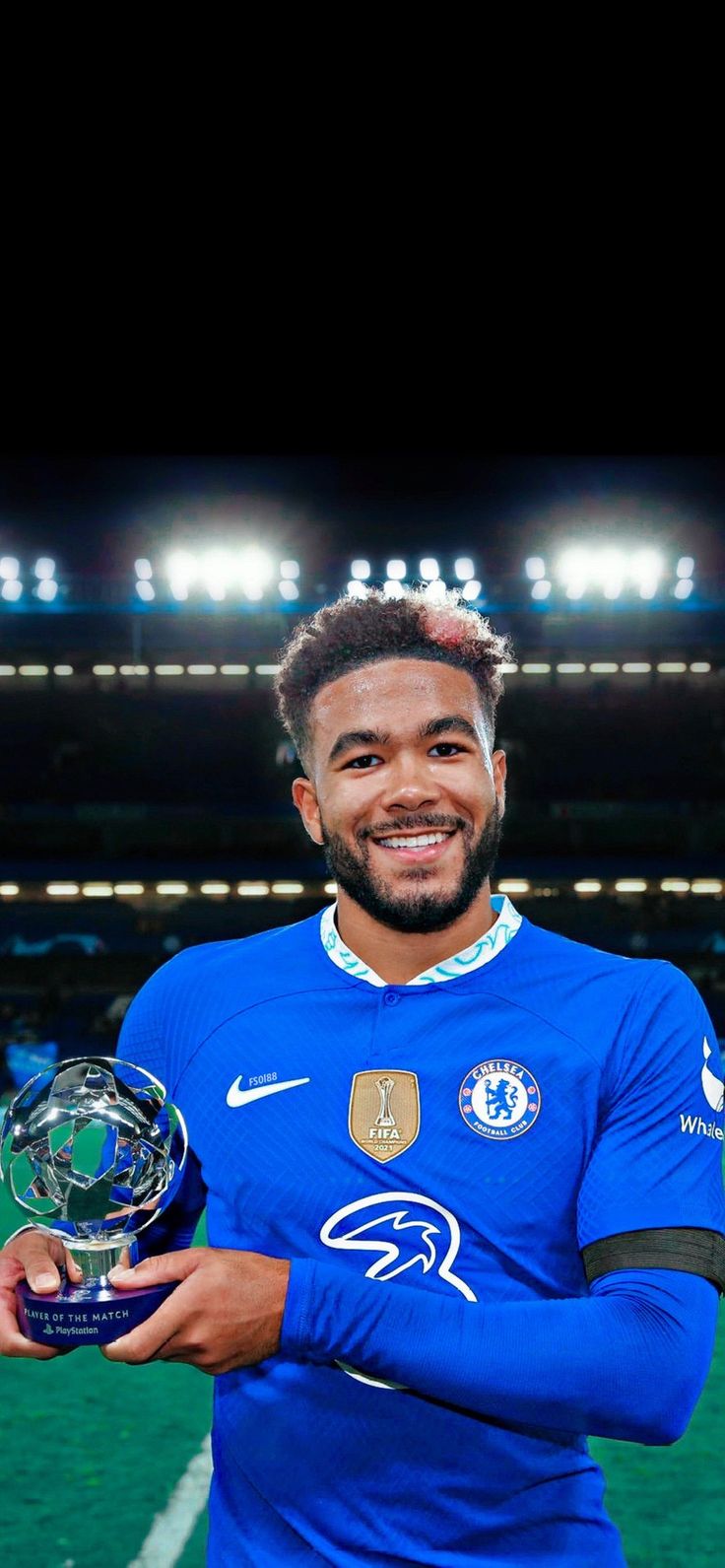 a man holding a soccer ball and trophy in front of a stadium filled with people