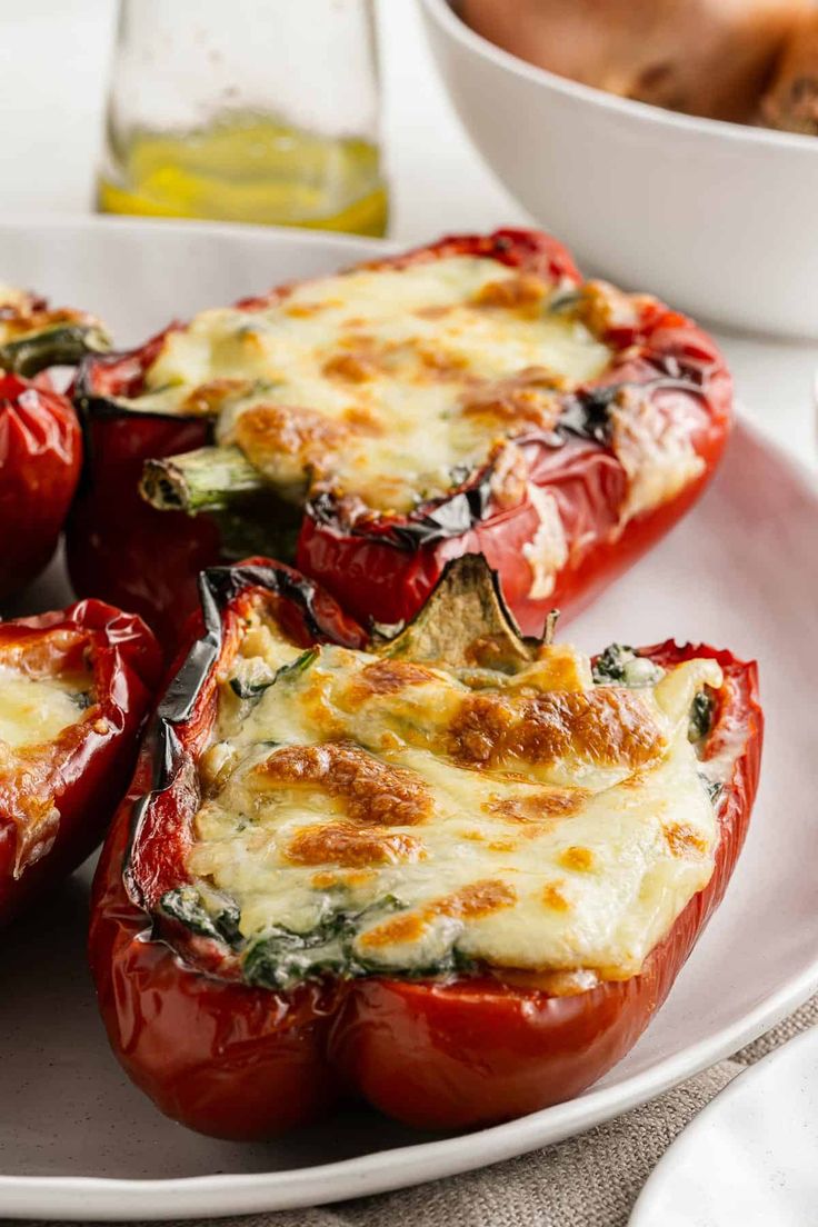 several stuffed red peppers on a plate with other food items in the bowl behind them