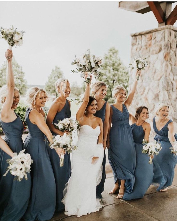 a group of women standing next to each other in front of a stone wall holding bouquets