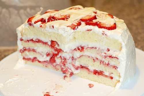 a piece of cake with strawberries on top is sitting on a plate and has one slice cut out