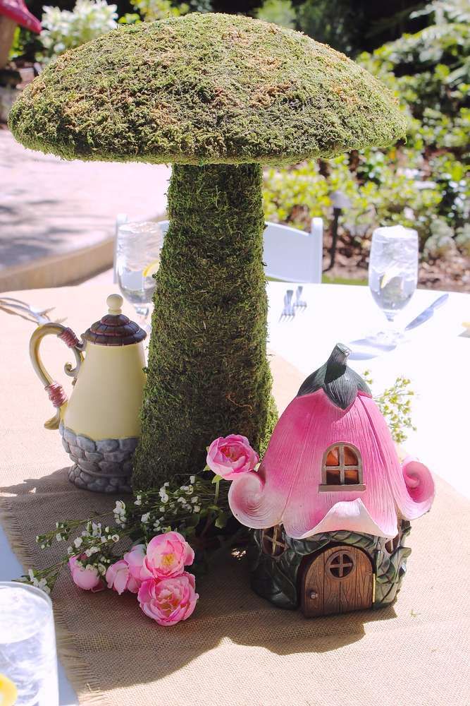 a table topped with a mushroom shaped planter next to a pink flower covered house