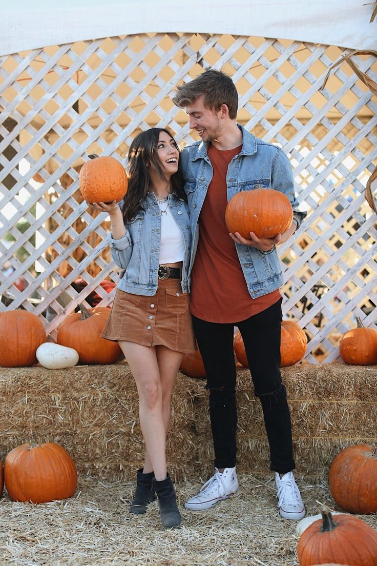 a man and woman standing next to each other in front of pumpkins