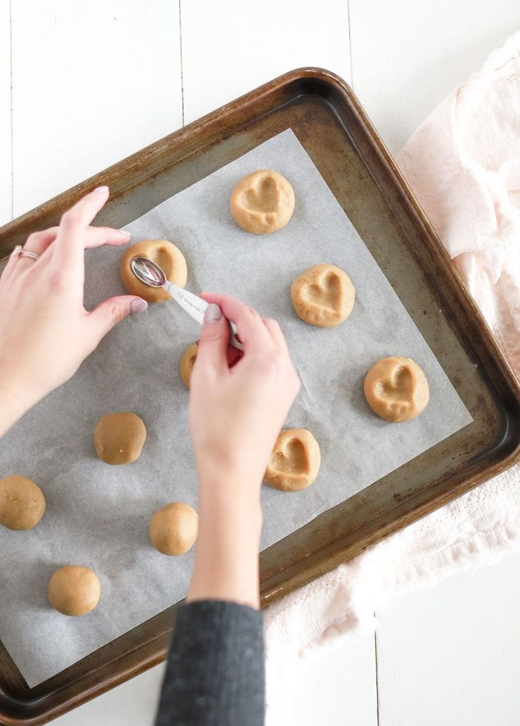 a person is making heart shaped cookies on a baking sheet