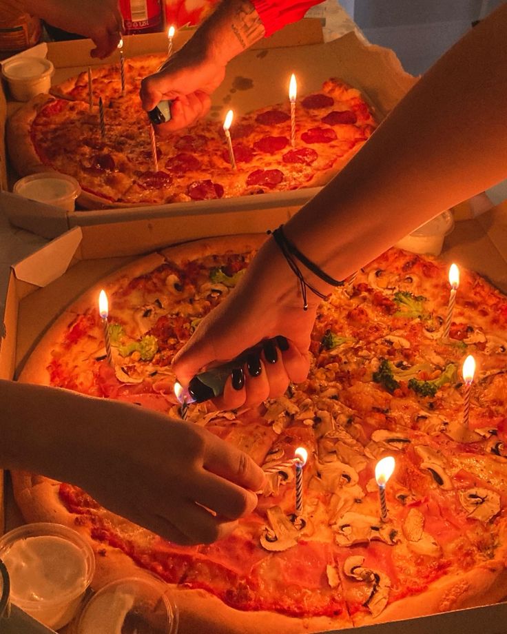 two people reaching for candles on top of a pizza in a box with many different toppings