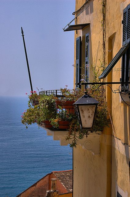 an old building with flowers in the window boxes and a view of the ocean behind it