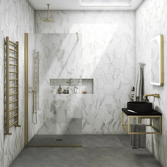 a white bathroom with gold accents and marble tiles on the walls, along with a walk in shower