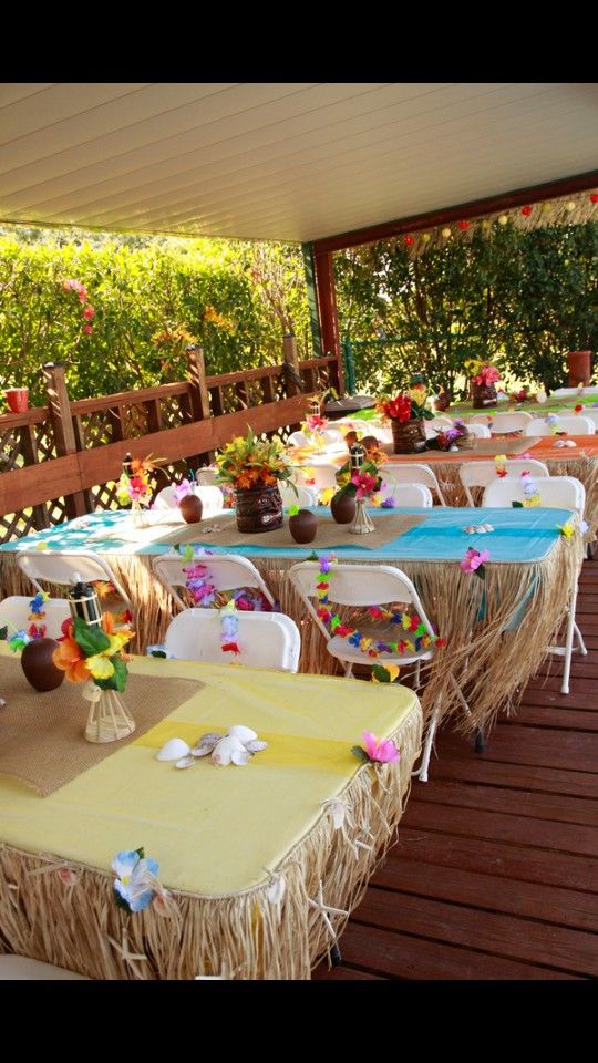 tables and chairs are set up on the deck for an outdoor party with flowers in vases