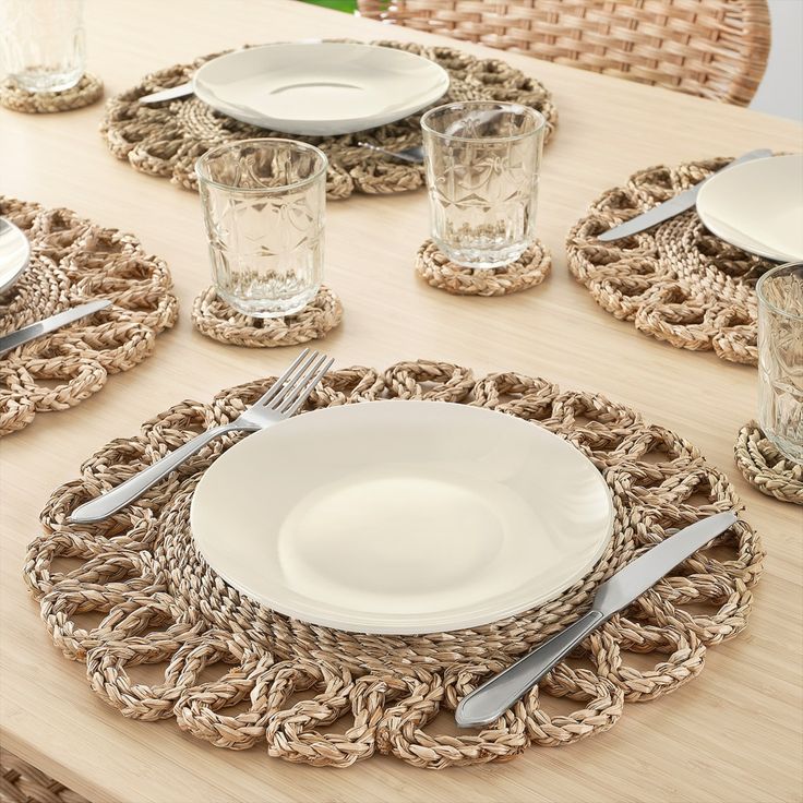 the table is set with plates and silverware on woven placemats, along with glass vases