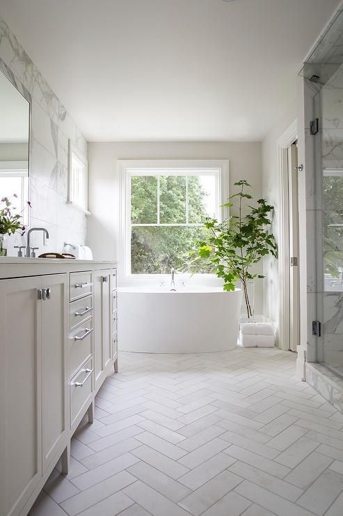 a white bathroom with a plant in the window and marble tile flooring on the walls