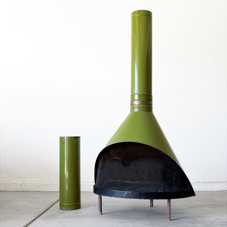 a large green stove sitting next to a tall cylinder on the ground in front of a white wall