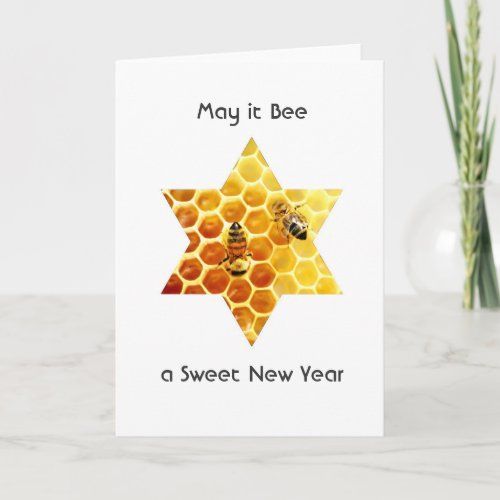 a happy new year greeting card with a bee and honeycombs on it, next to a vase filled with flowers