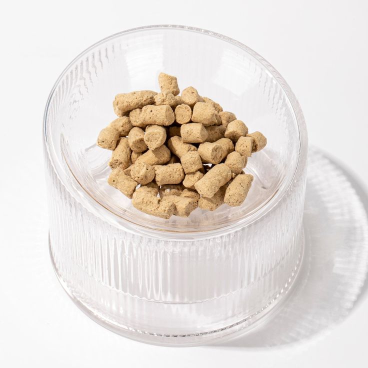 a clear bowl filled with dog food on top of a white table