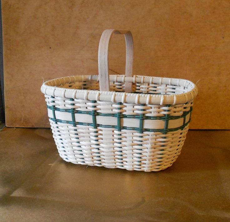 a white and green basket sitting on top of a wooden table next to a wall