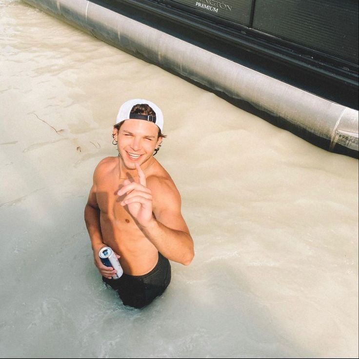 a shirtless man sitting in the water with his hand on his hip and smiling