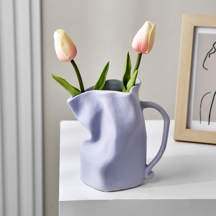 three tulips in a blue vase next to a framed drawing and a frame