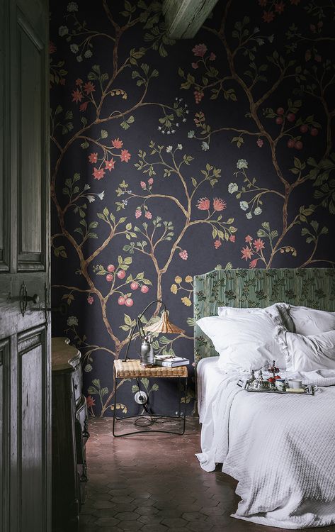 a bed sitting in a bedroom next to a wallpaper covered in leaves and flowers