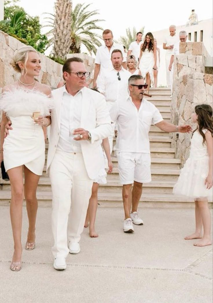 a group of people that are walking down some steps together in white outfits and tuxedos