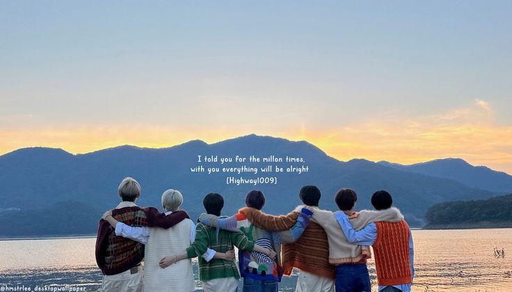 four people standing on the beach with their arms around each other looking out at mountains