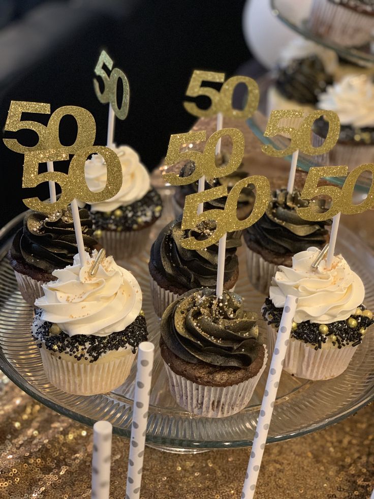 cupcakes with white frosting and gold numbers are on a glass platter