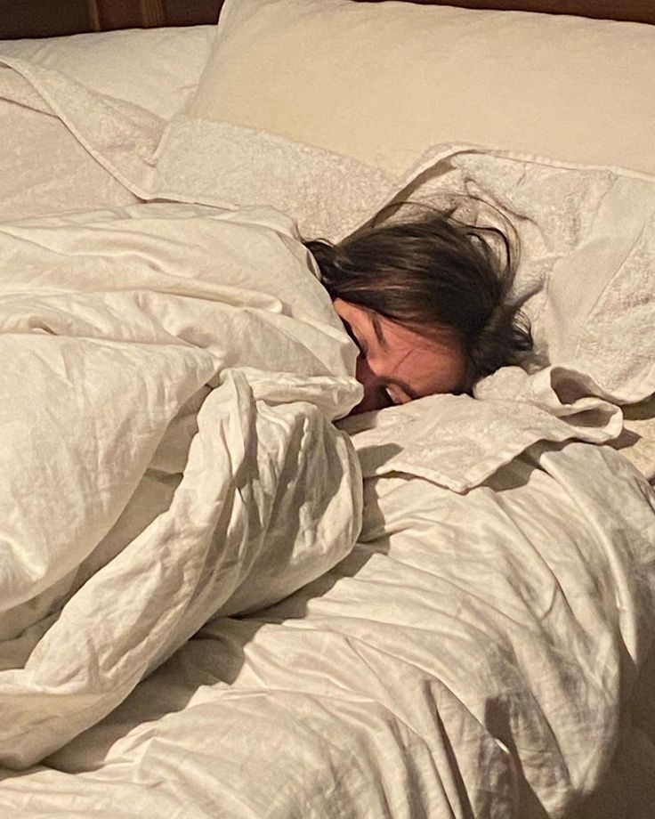 a woman is sleeping in bed with her head tucked under the covers and covering herself