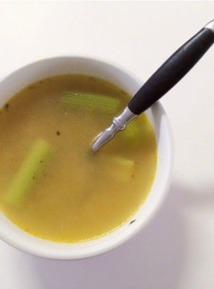 a white bowl filled with soup and a black spoon in the cup next to it