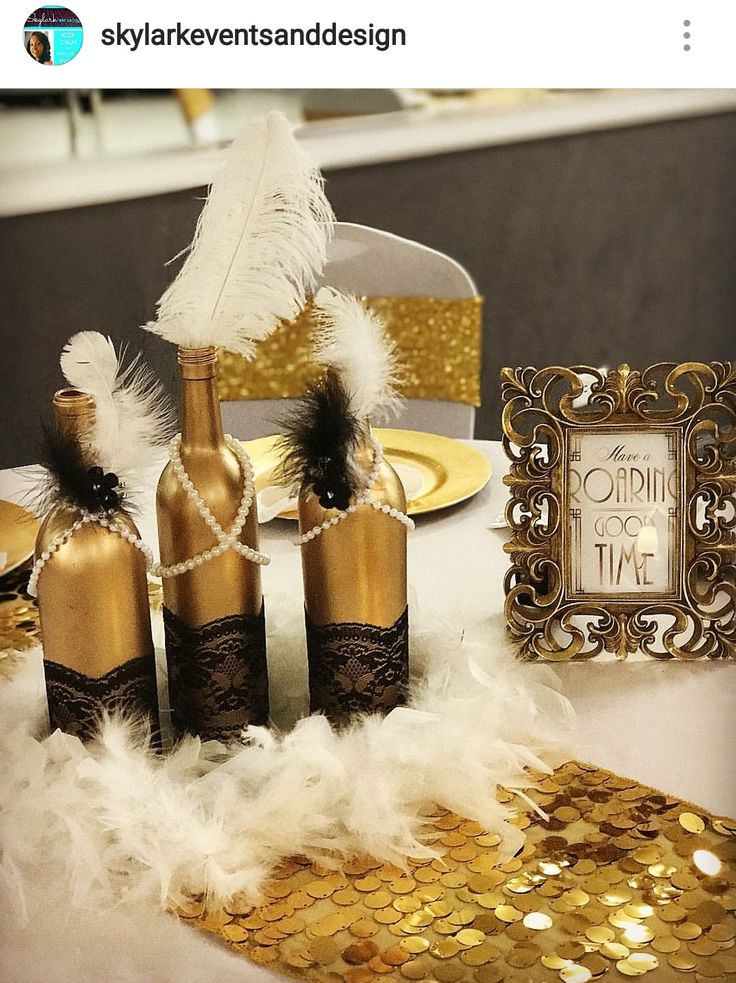 a table with gold and white decorations on it, including wine bottles in the shape of feathers