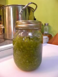 a jar filled with green stuff sitting on top of a counter next to a pot