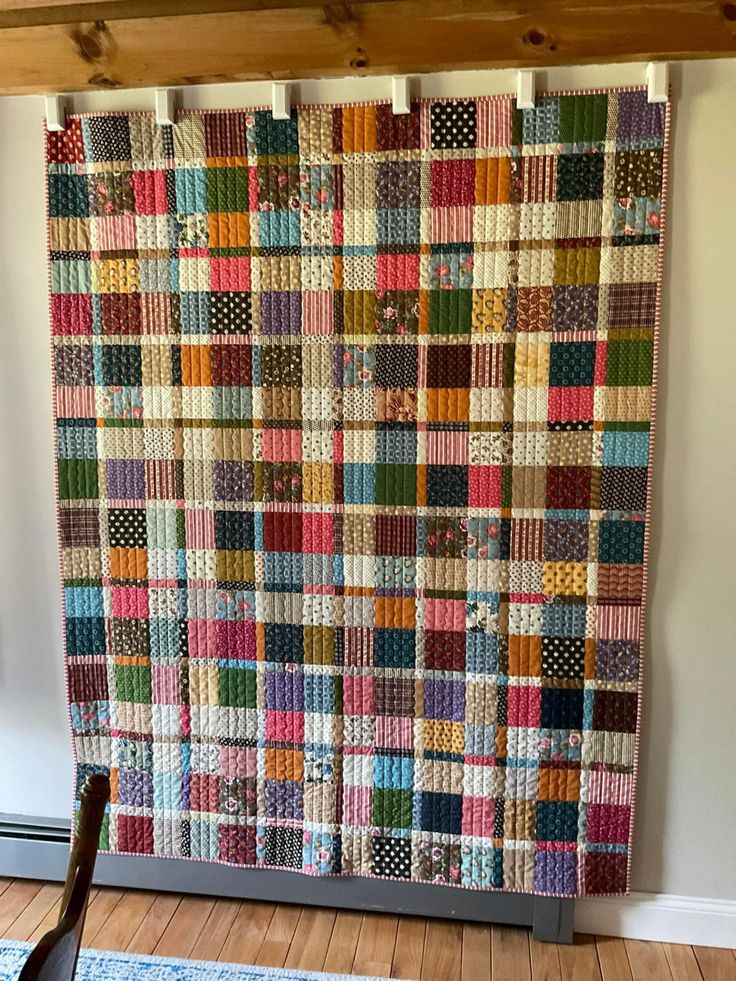 a multicolored quilt hanging on the wall next to a rocking chair and rug