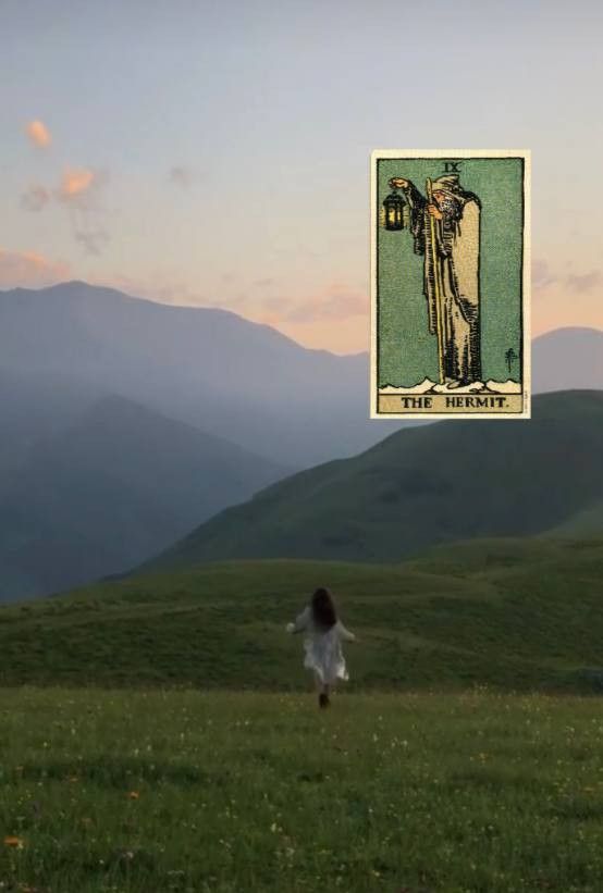 a woman walking across a lush green field under a sky with mountains in the background