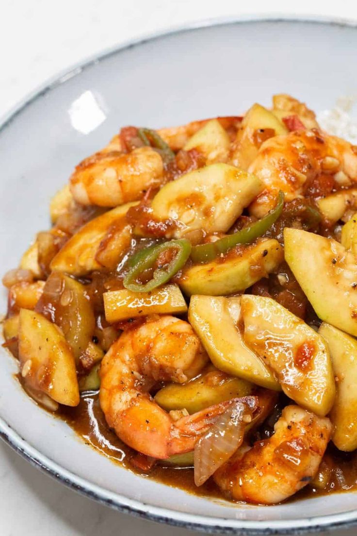 a white plate topped with shrimp and veggies covered in sauce next to rice