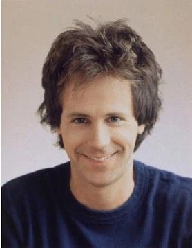 a man smiling and wearing a blue shirt with his hair in a messy updo