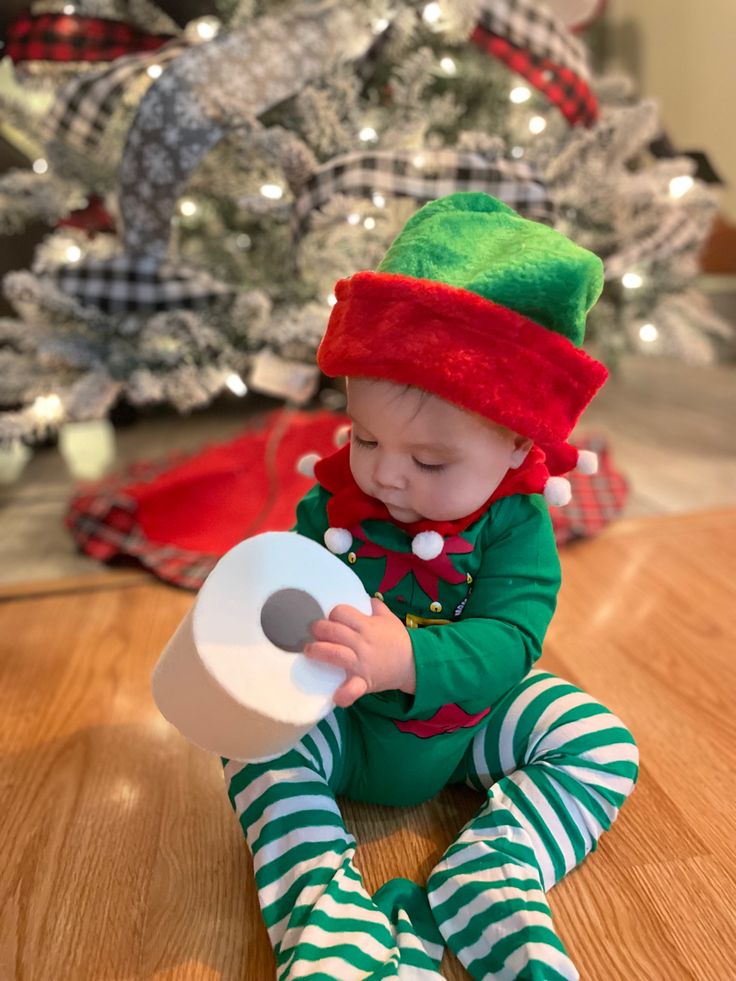 a small child sitting on the floor with a roll of toilet paper in front of a christmas tree