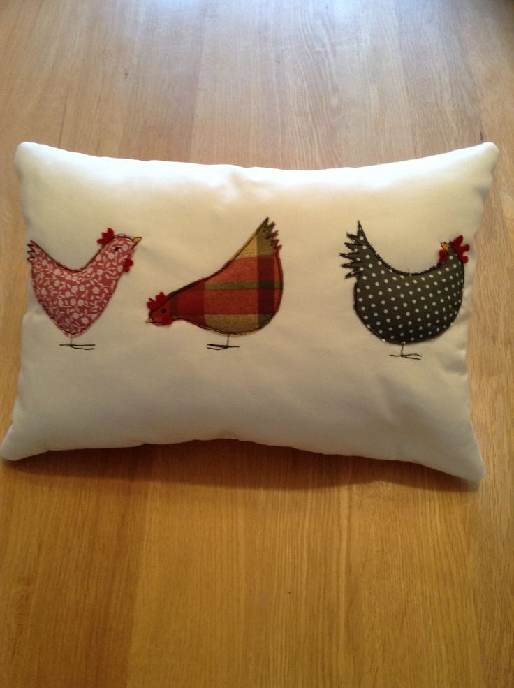 three chickens embroidered on a white pillow sitting on a wooden floor in front of a window