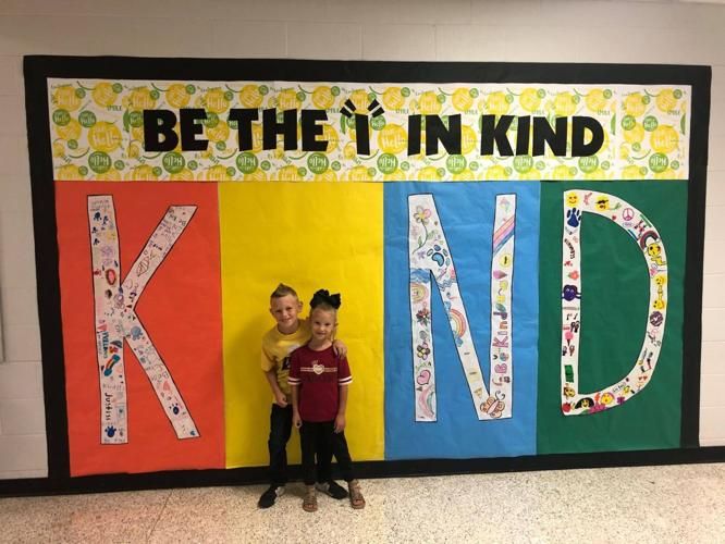 two children standing in front of a bulletin board that says be the i in kind