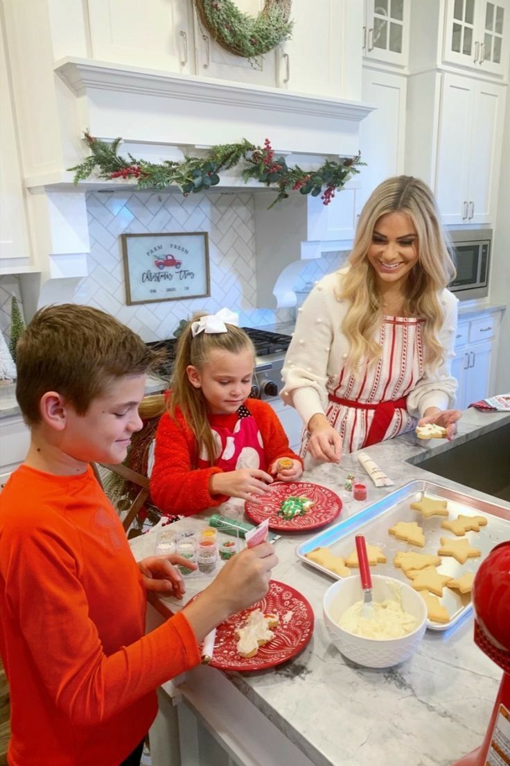 a woman and two children making cookies in the kitchen with christmas decorations on the counter