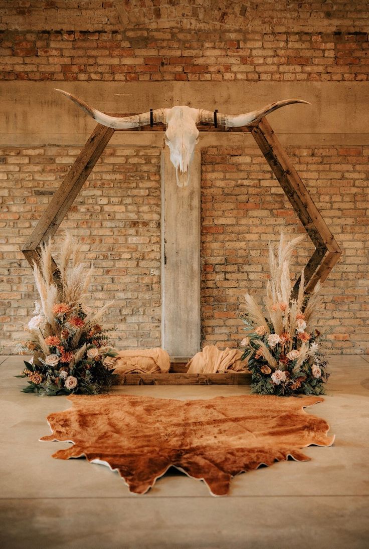 a cow skull on display in front of a brick wall with flowers and greenery