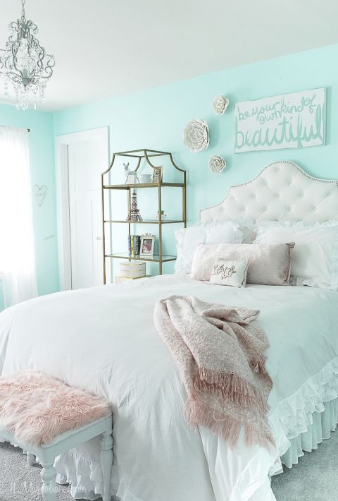 a white bed sitting in a bedroom next to a chandelier and pillows on top of it