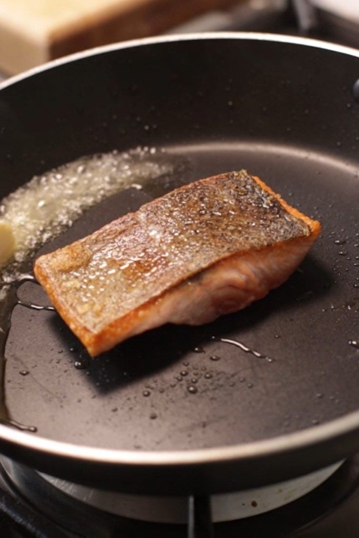 a piece of fish is cooking in a frying pan on the stove with oil