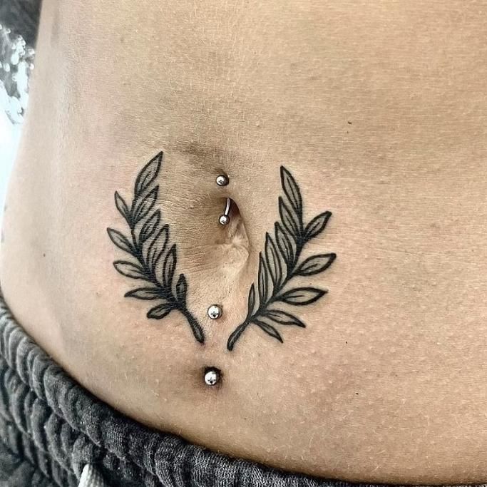 a woman's stomach with a tattoo design on the belly and leaves around it