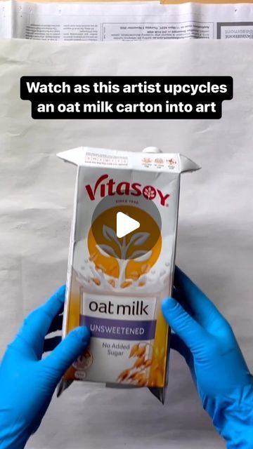 a person in blue gloves holding up a carton of oat milk with the caption, watch as this artist upcycles an oat milk carton into art