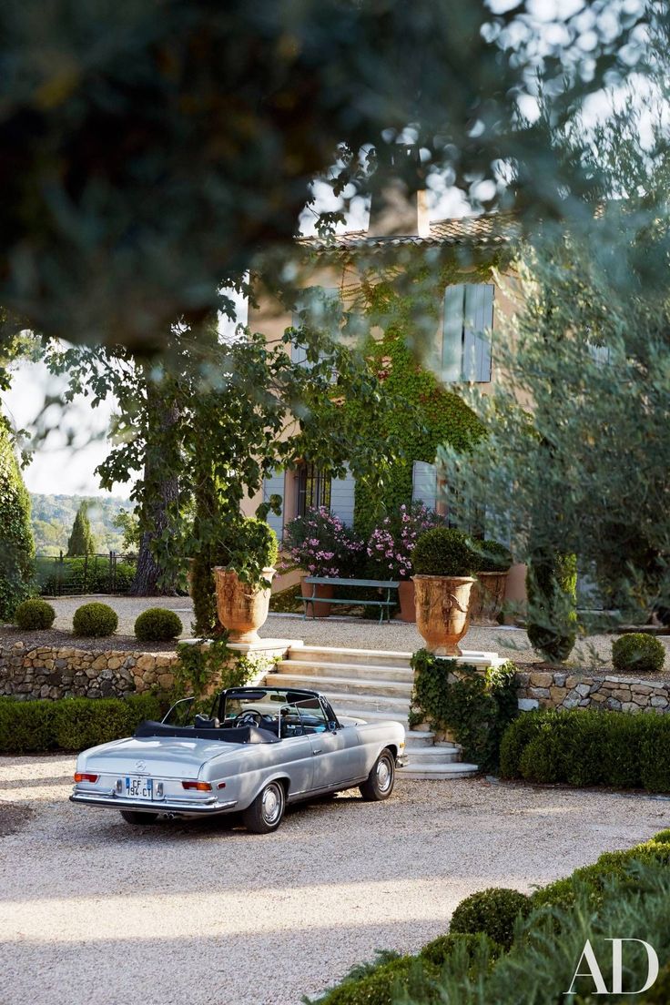 an old car parked in front of a house with potted plants on the driveway