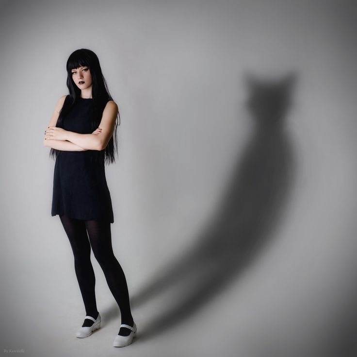 a woman standing with her arms crossed in front of the shadow of a cat's head