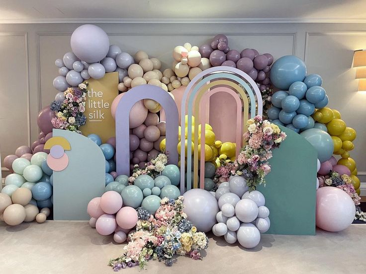 balloons and flowers are arranged on the floor in front of a backdrop made of archs